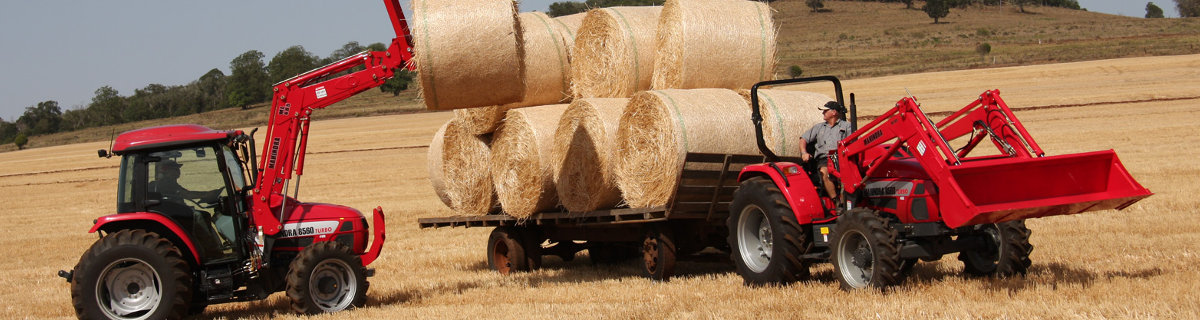 Two tractors hauling and loading hay bales